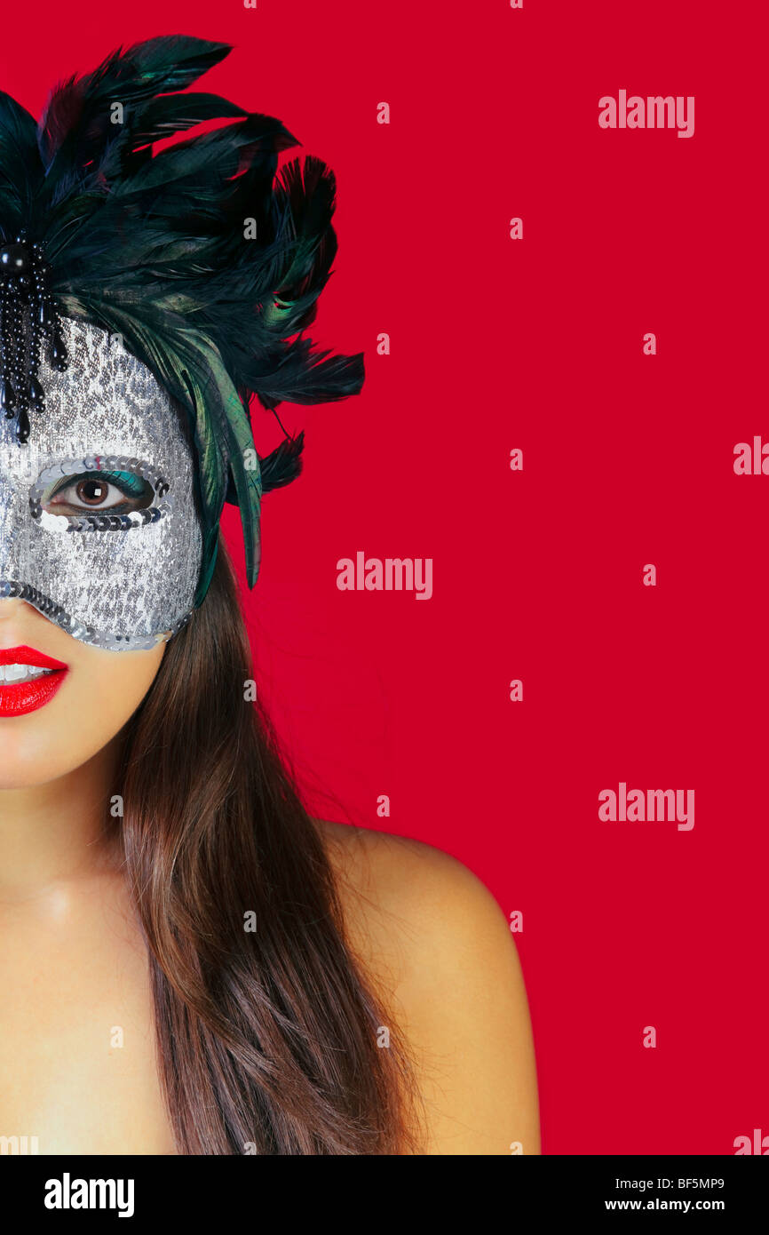 Beautiful brunette woman wearing a masqurade mask against a red background. Stock Photo