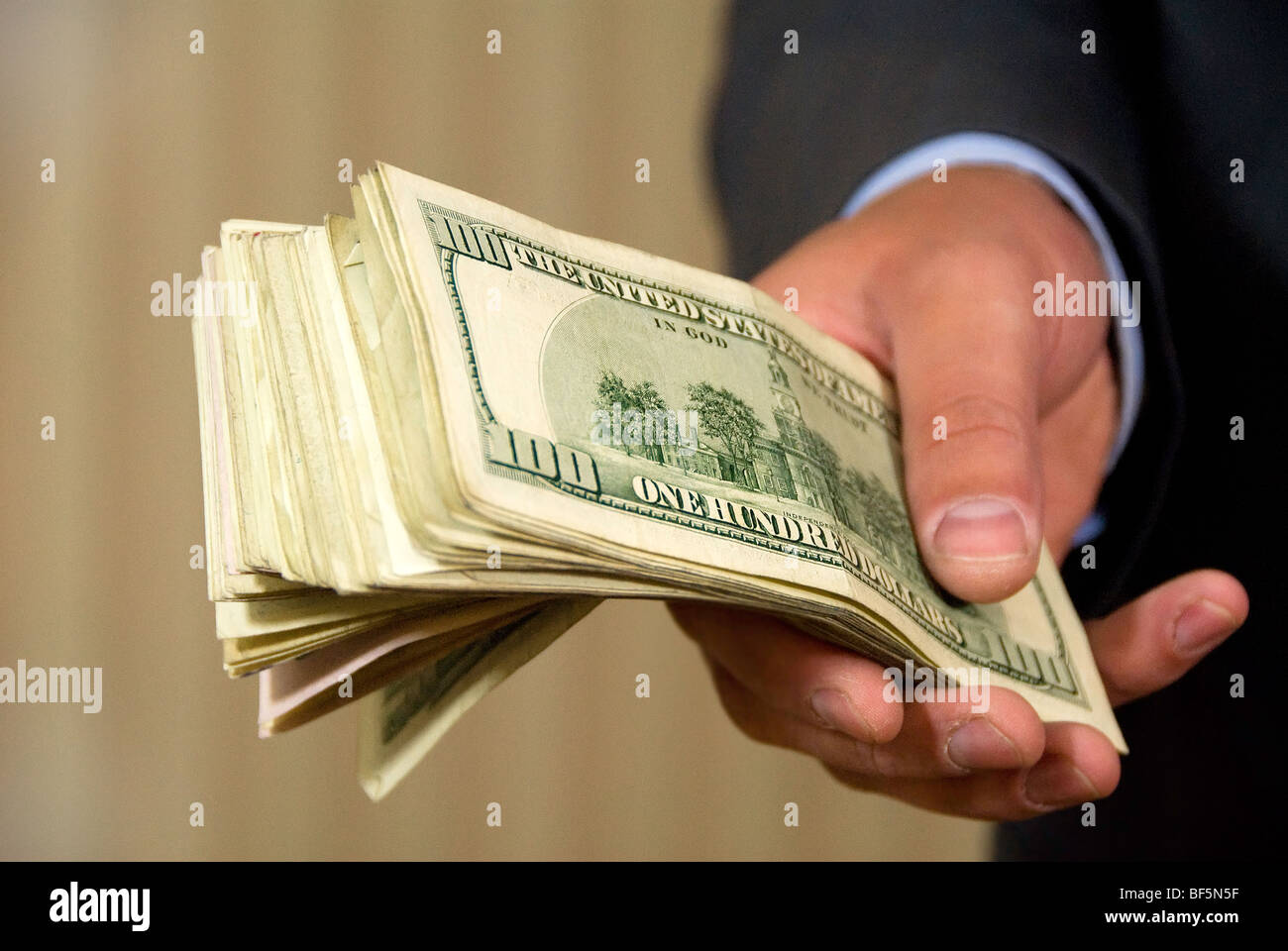a hand giving a stack of 100 dollar bills Stock Photo