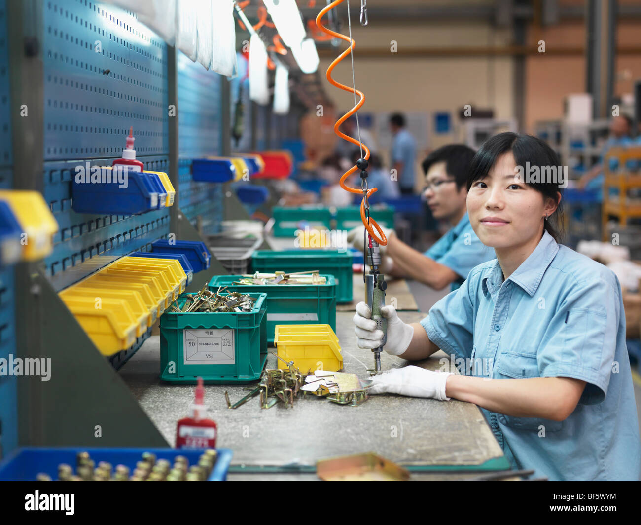 A woman bolting parts of hardware together in a factory assembly line. Stock Photo