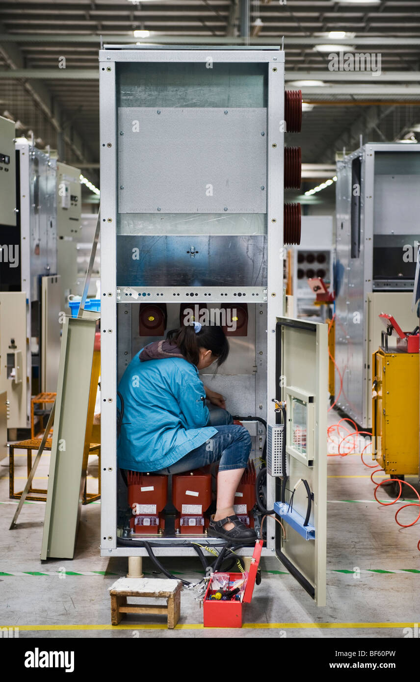 A factory worker installing a part of an electrical panel in an assembly line Stock Photo