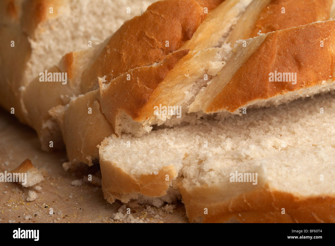 close up of fresh white crusty bloomer loaf cut into rough slices on a wooden block Stock Photo