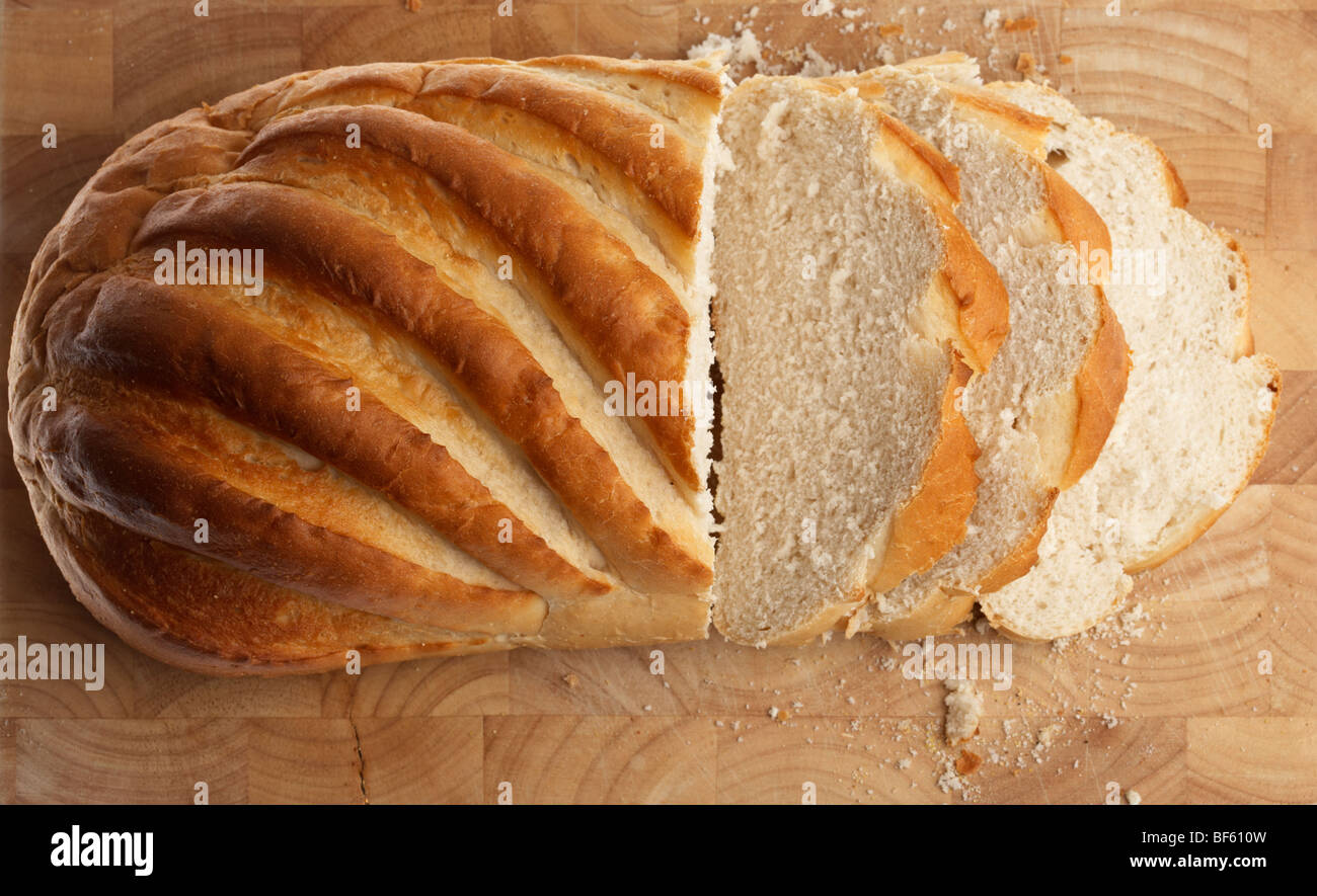 fresh white crusty bloomer loaf cut into rough slices on a wooden block Stock Photo