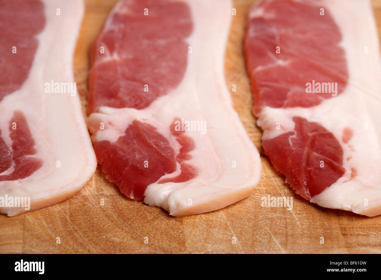 three strips of raw back bacon from organic british saddleback pigs reared in ireland laid out on a wooden butchers block Stock Photo