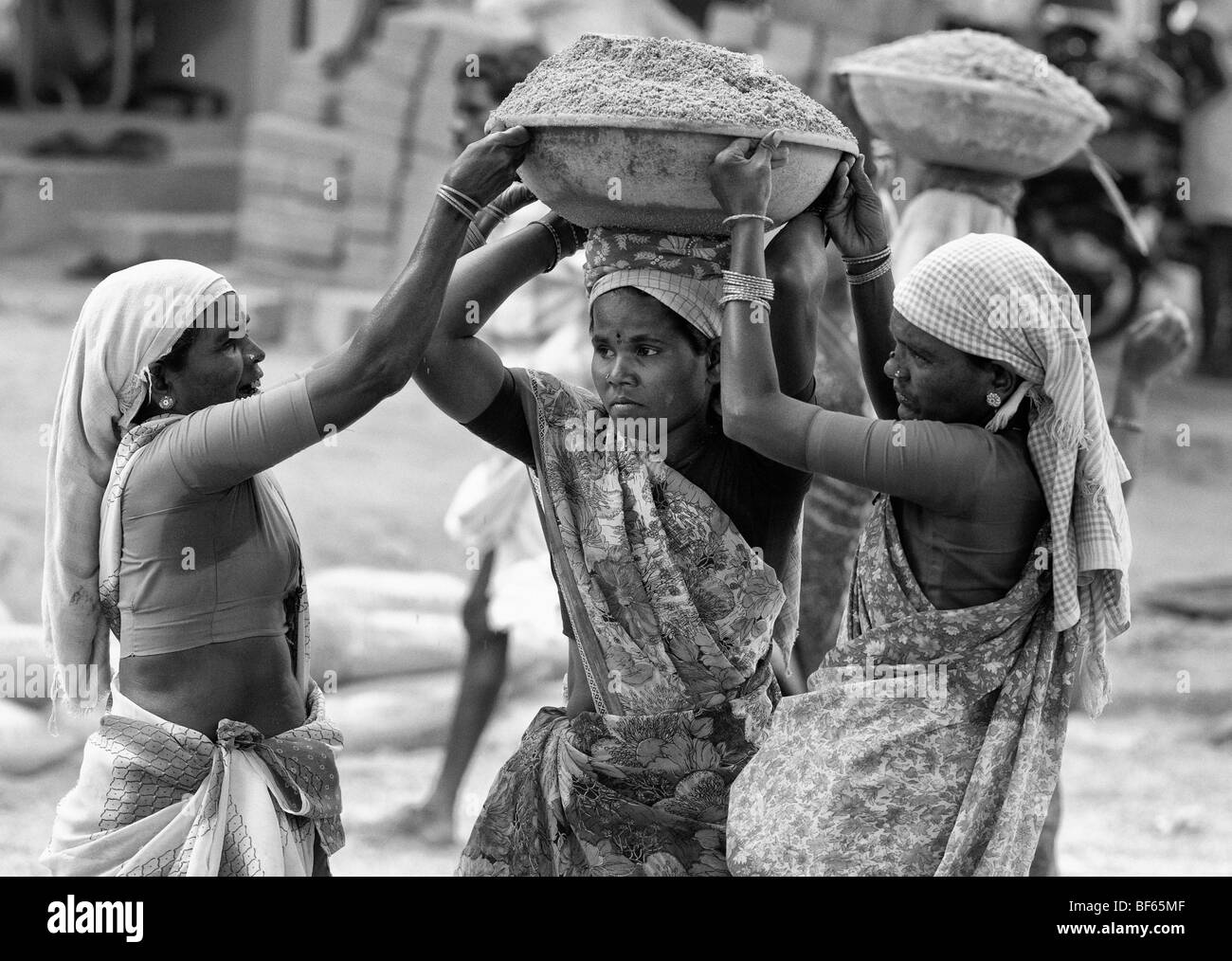 indian women working on the roads, lifting and carrying sand in a bowl on their heads. Puttaparthi, Andhra Pradesh, India. Monochrome Stock Photo