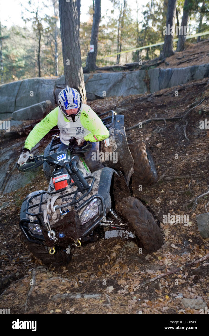 Man rides all-terrain vehicle (ATV) downhill on steep terrain in woods. Trial off-road biking Stock Photo