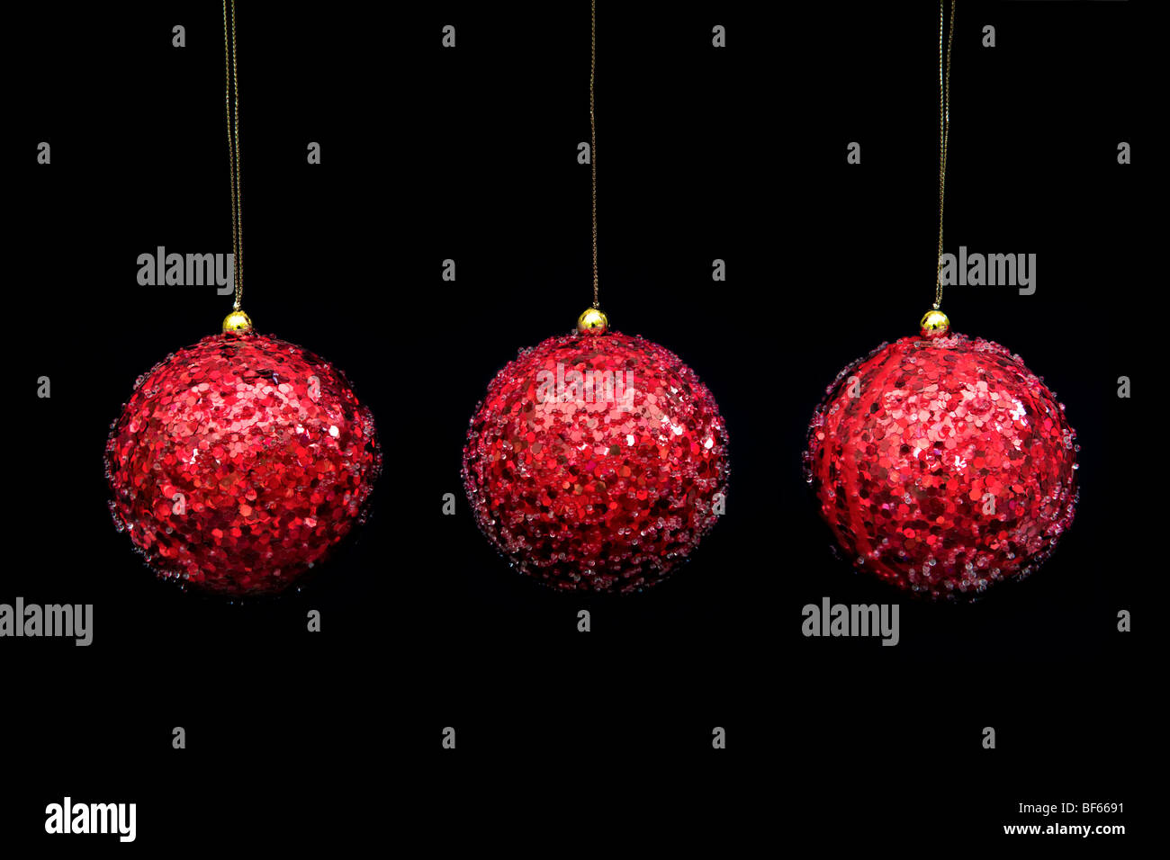 Three red coloured decorative baubles in a row hanging with gold thread against a black background Stock Photo