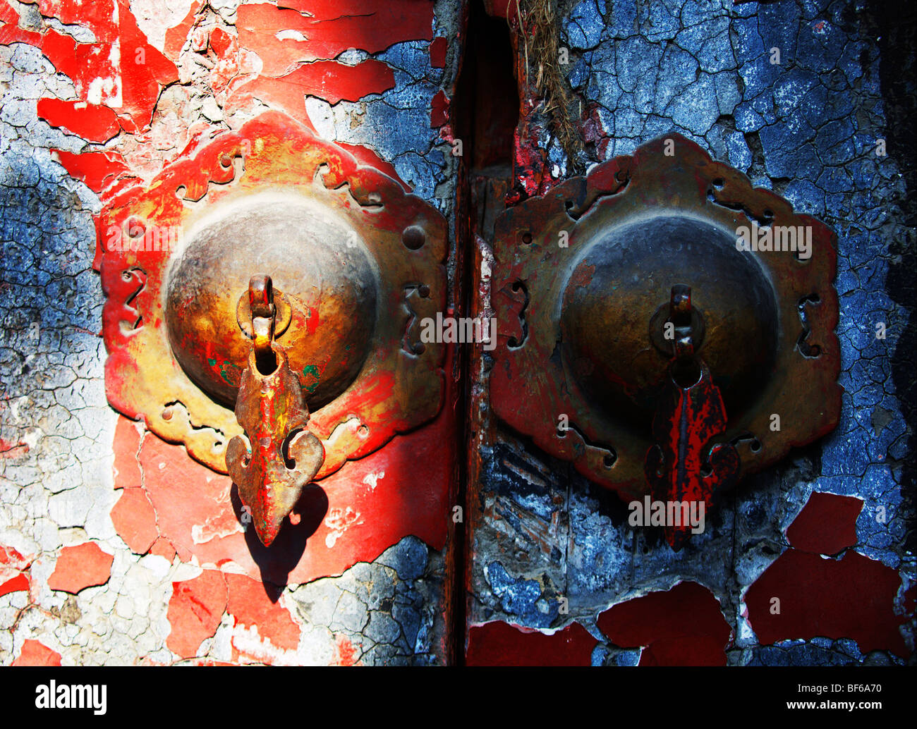 Old door handle on faded red door of traditional courtyard house in