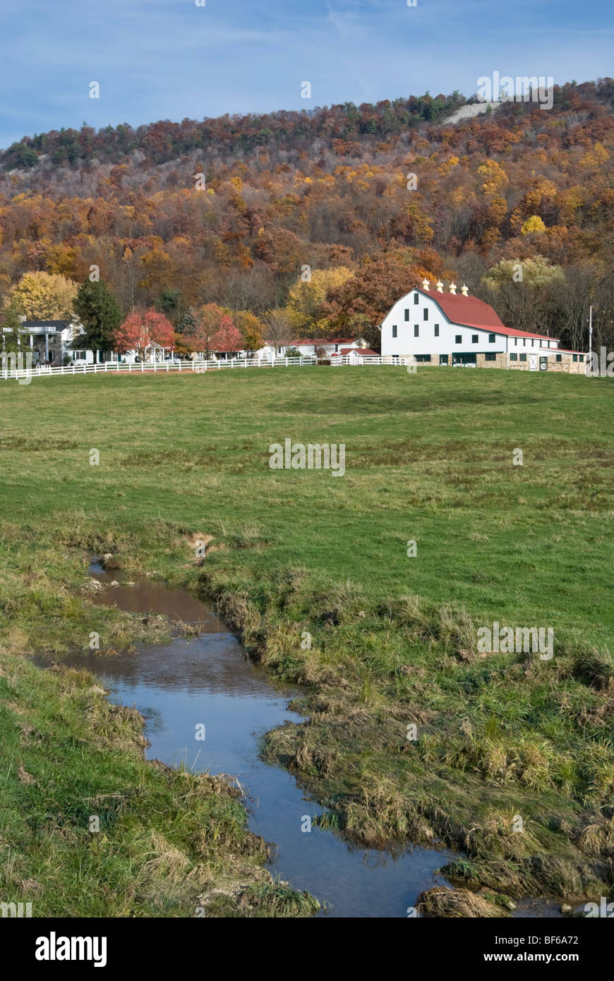 Stock photo of white barn against fall mountainside in Pennsylvania, with run off stream flowing in foreground. Stock Photo