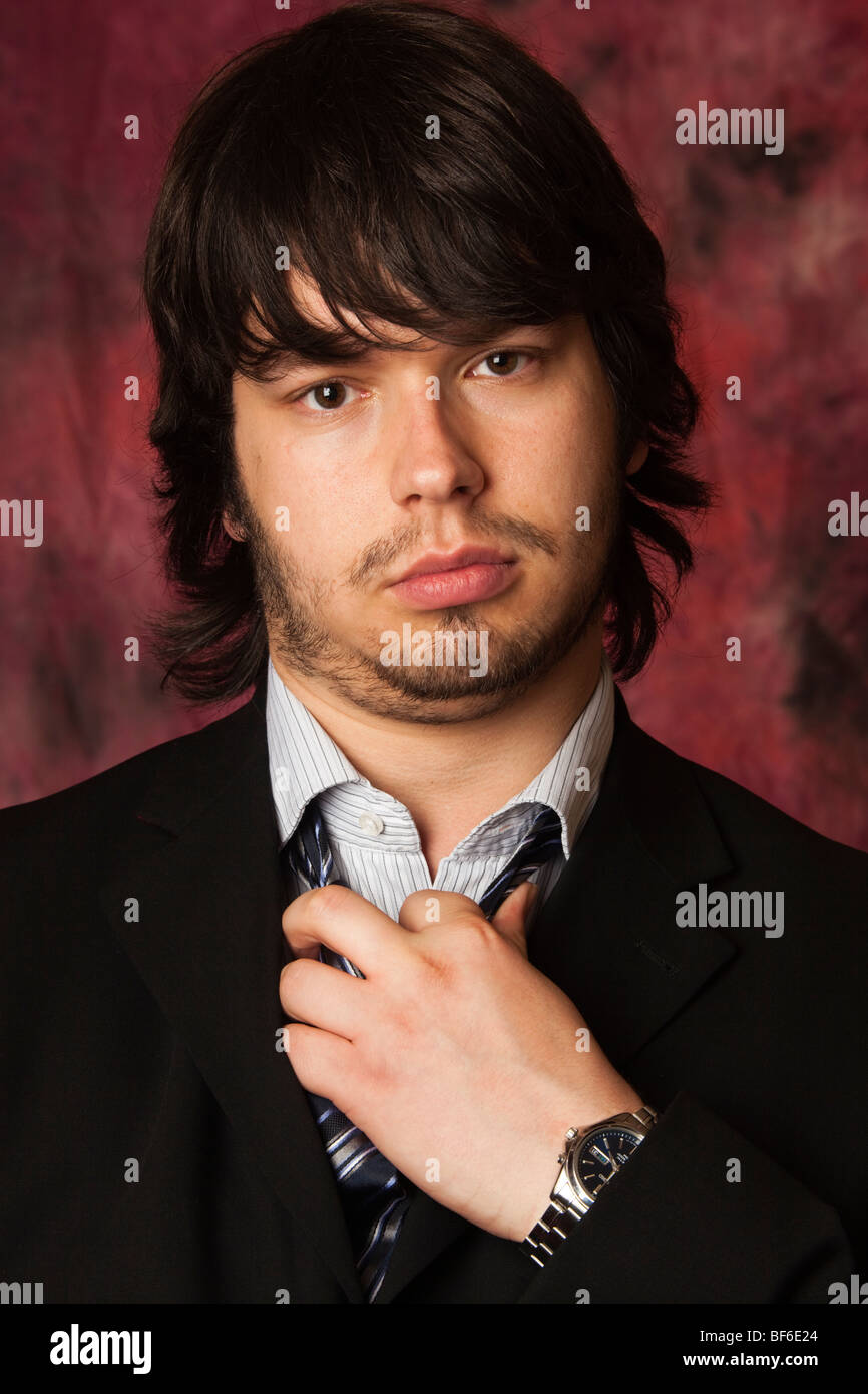 Young man looking sullen in a dark suit loosening his tie Stock Photo
