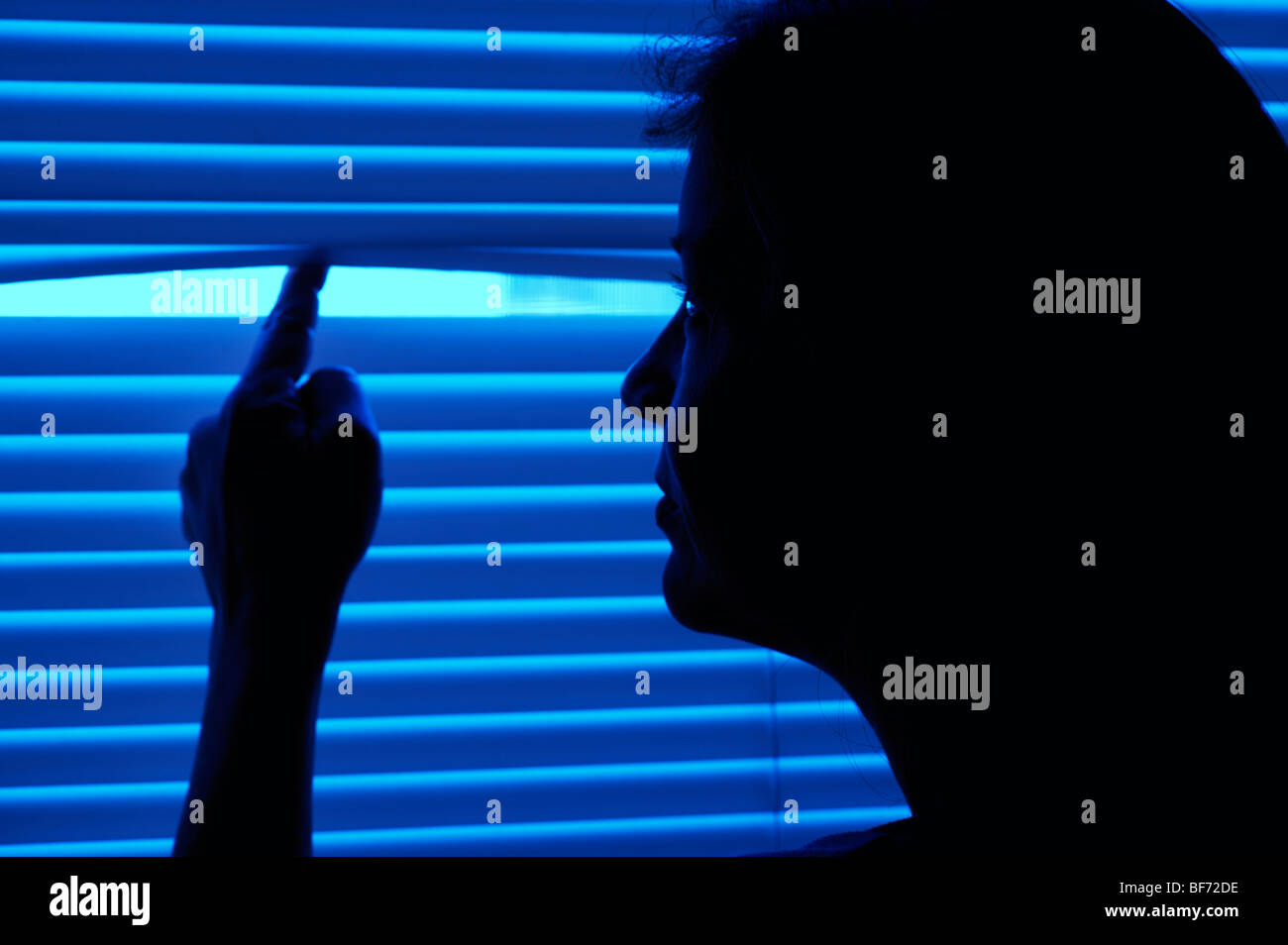 silhouetted woman peering thorough blinds Stock Photo