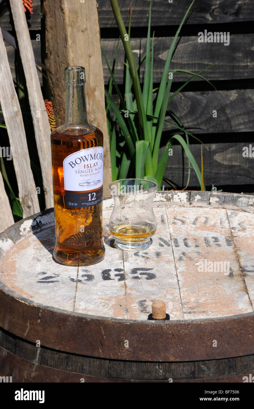 An open bottle of Bowmore Islay single malt whisky and a glass on an old barrel. Stock Photo