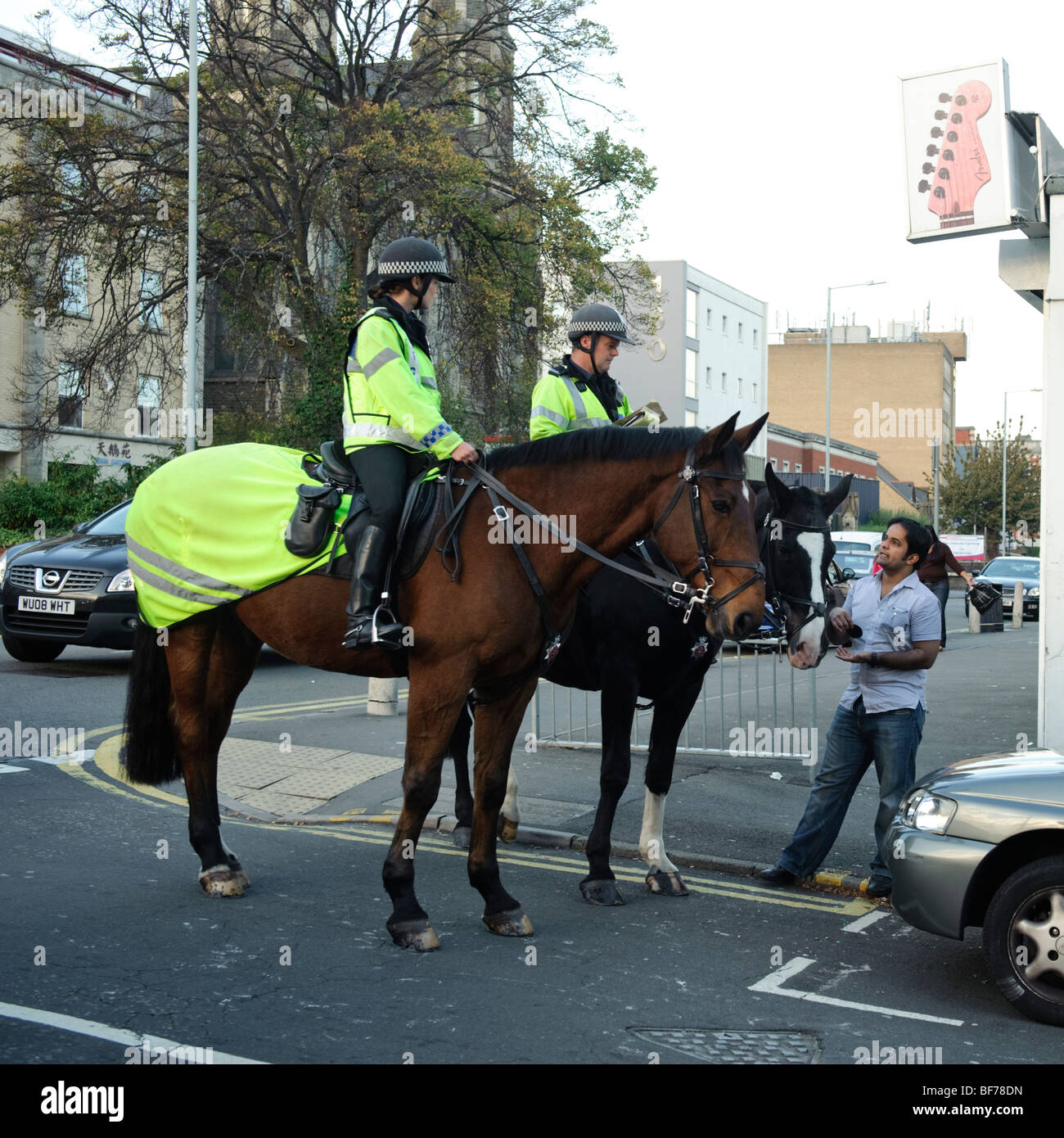 Two mounted police officers cops on horseback talking to a member of the public in Swansea city centre, Wales UK Stock Photo