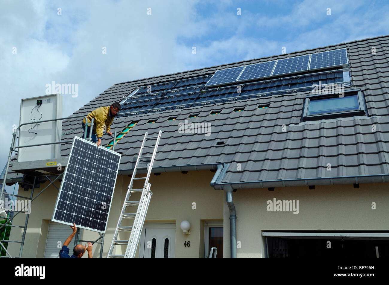 workmen installing photovoltaic solar panels on the roof of a private house Stock Photo