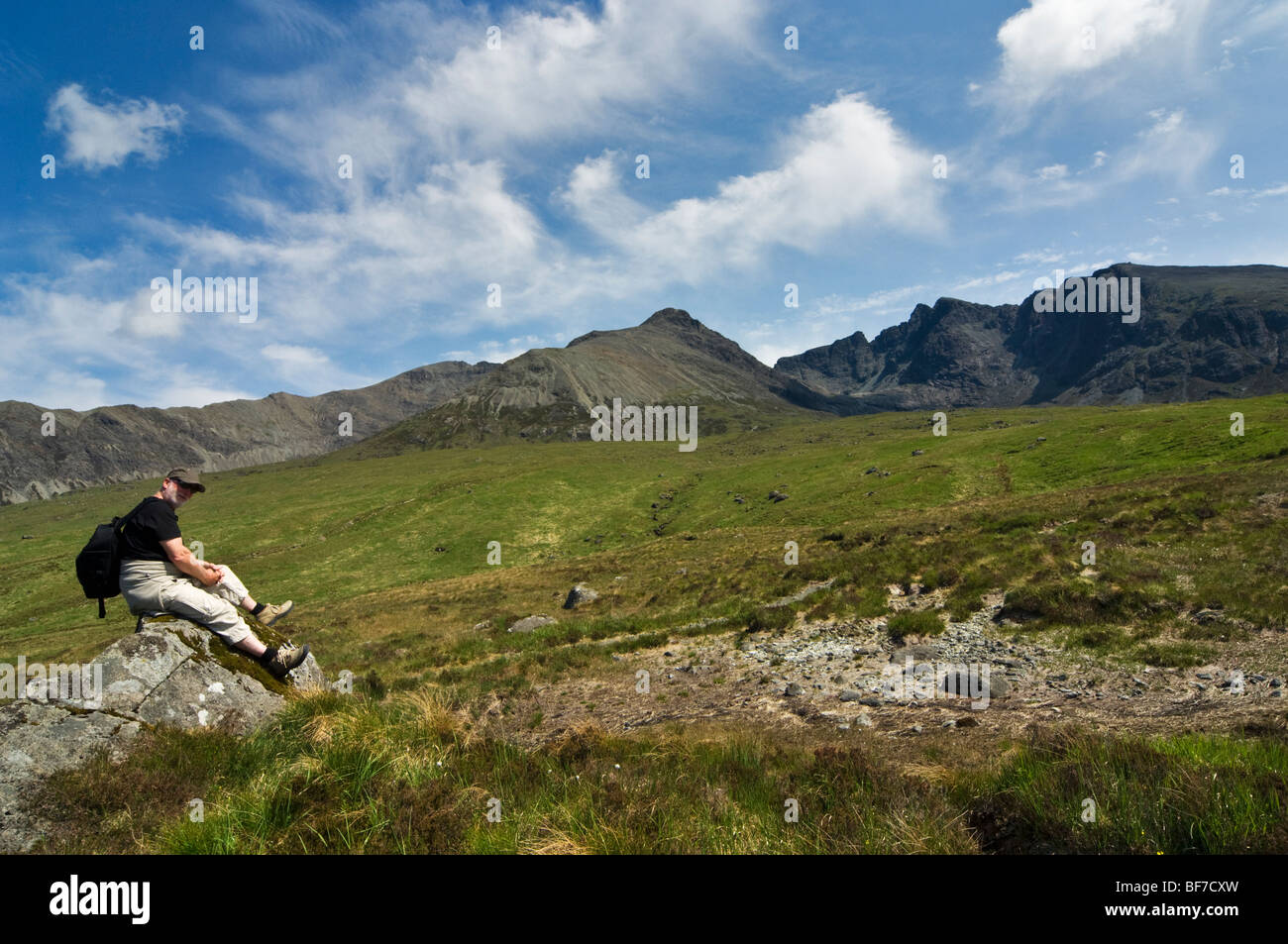 Tourist sitting on a rock with the Cullin Hills (Black Cullin on right) in the background, Isle of Sky, Scotland, UK Stock Photo
