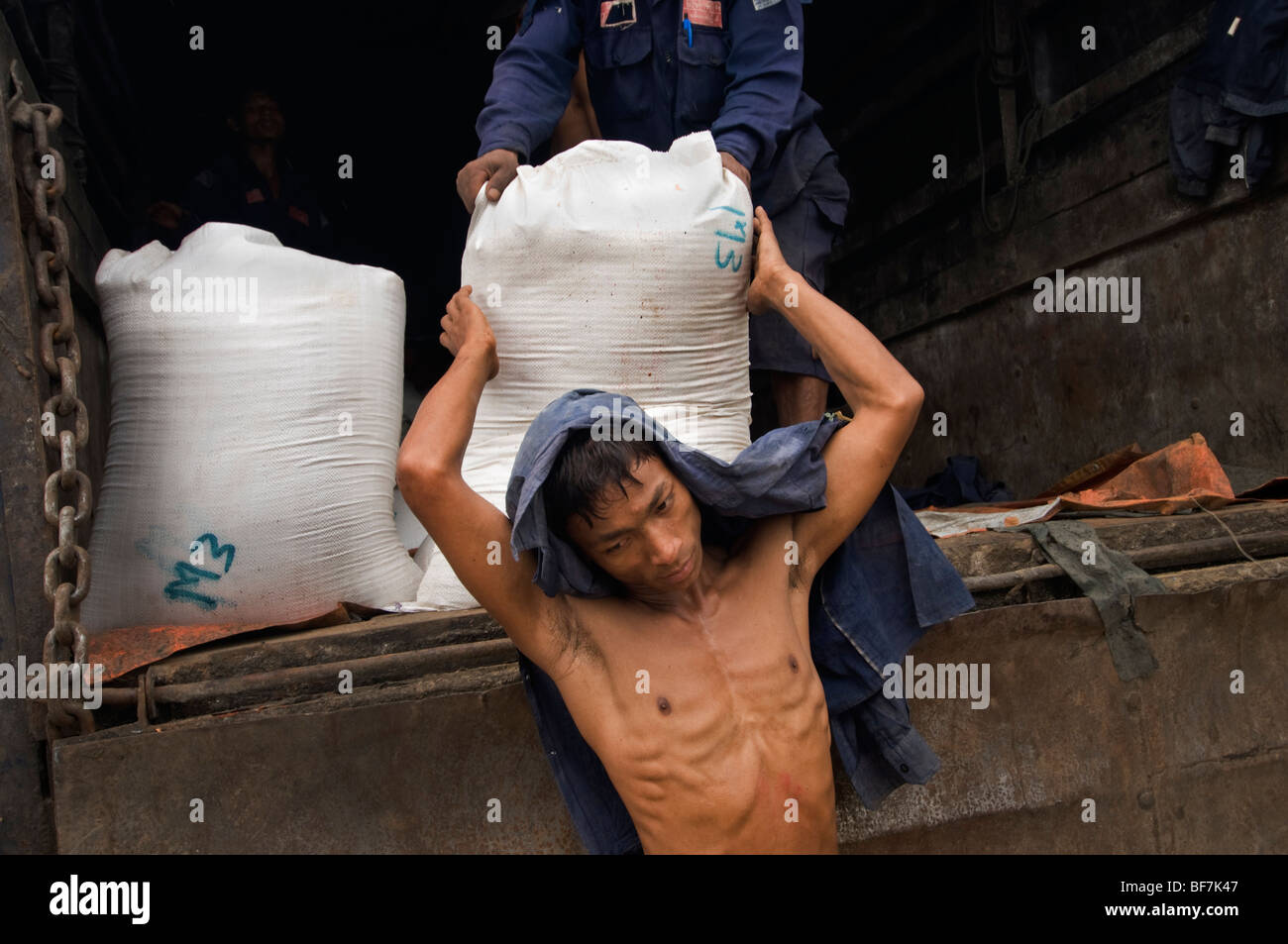 A shirtless Burmese worker unloading sacks off a truck at the Yangon ...