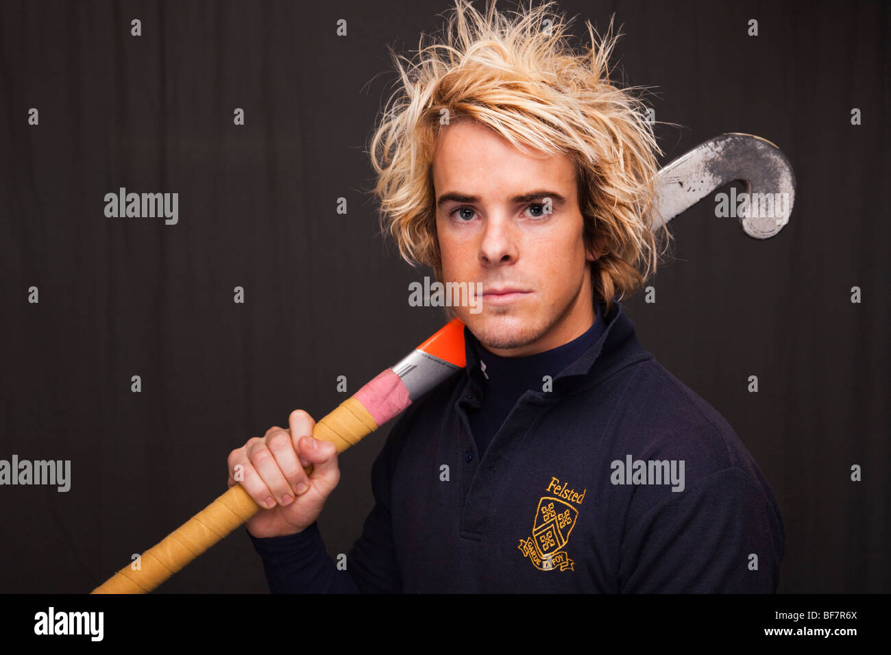 Head and shoulders portrait of a young man with a determined expression wearing a hockey shirt with a stick over his shoulder. UK Stock Photo