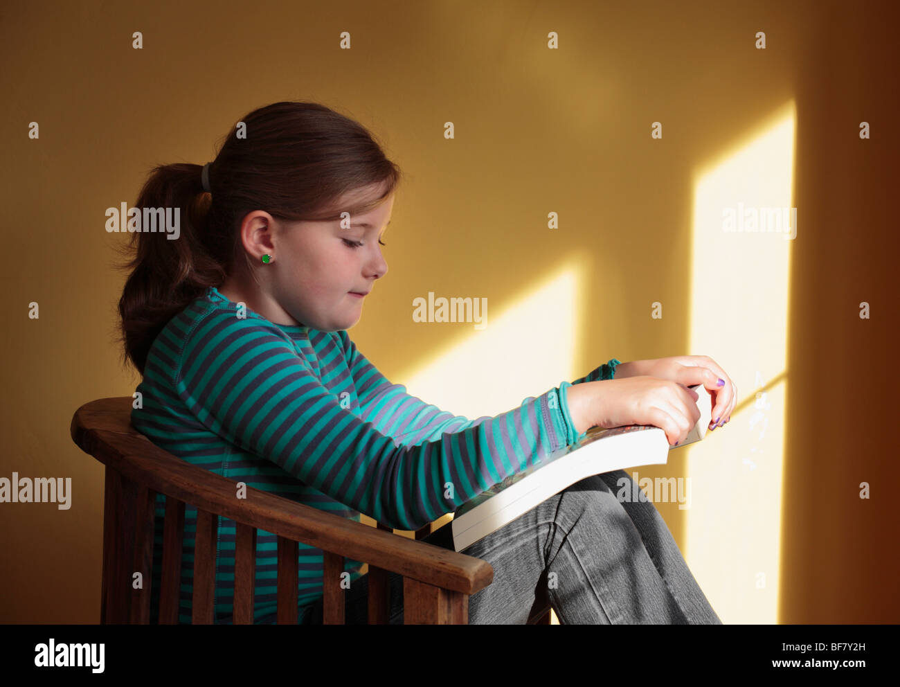 Ten year old girl reading a book by the light from a window Stock Photo