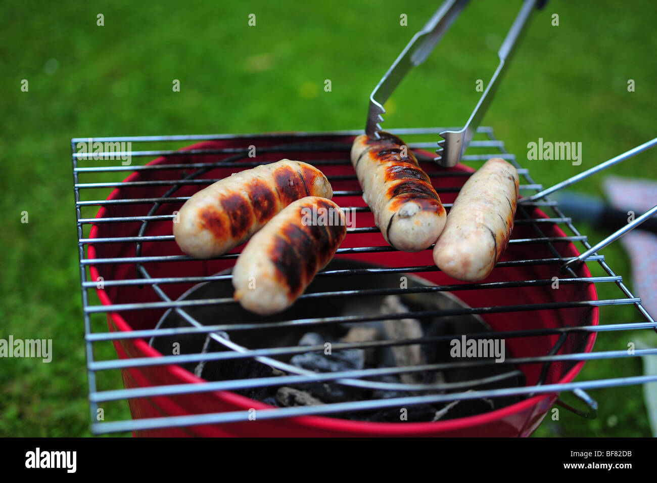 Sausages cooking on a barbeque BBQ in a garden in Devon, UK Stock Photo