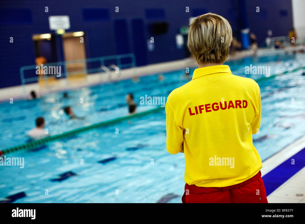 Female lifeguard watching swimmers at an indoor swimming pool in the UK
