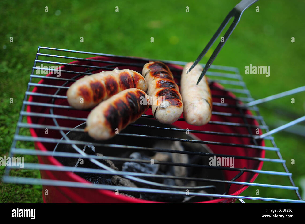Sausages cooking on a barbeque BBQ in a garden in Devon, UK Stock Photo