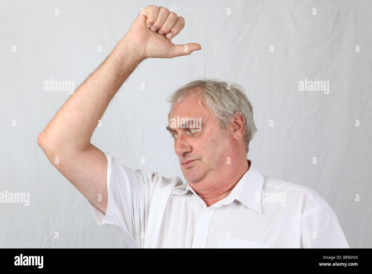 Mid 60s retired grey haired man sniffing smelling armpit checking for stale sour underarm body odour odor poor personal hygiene Stock Photo