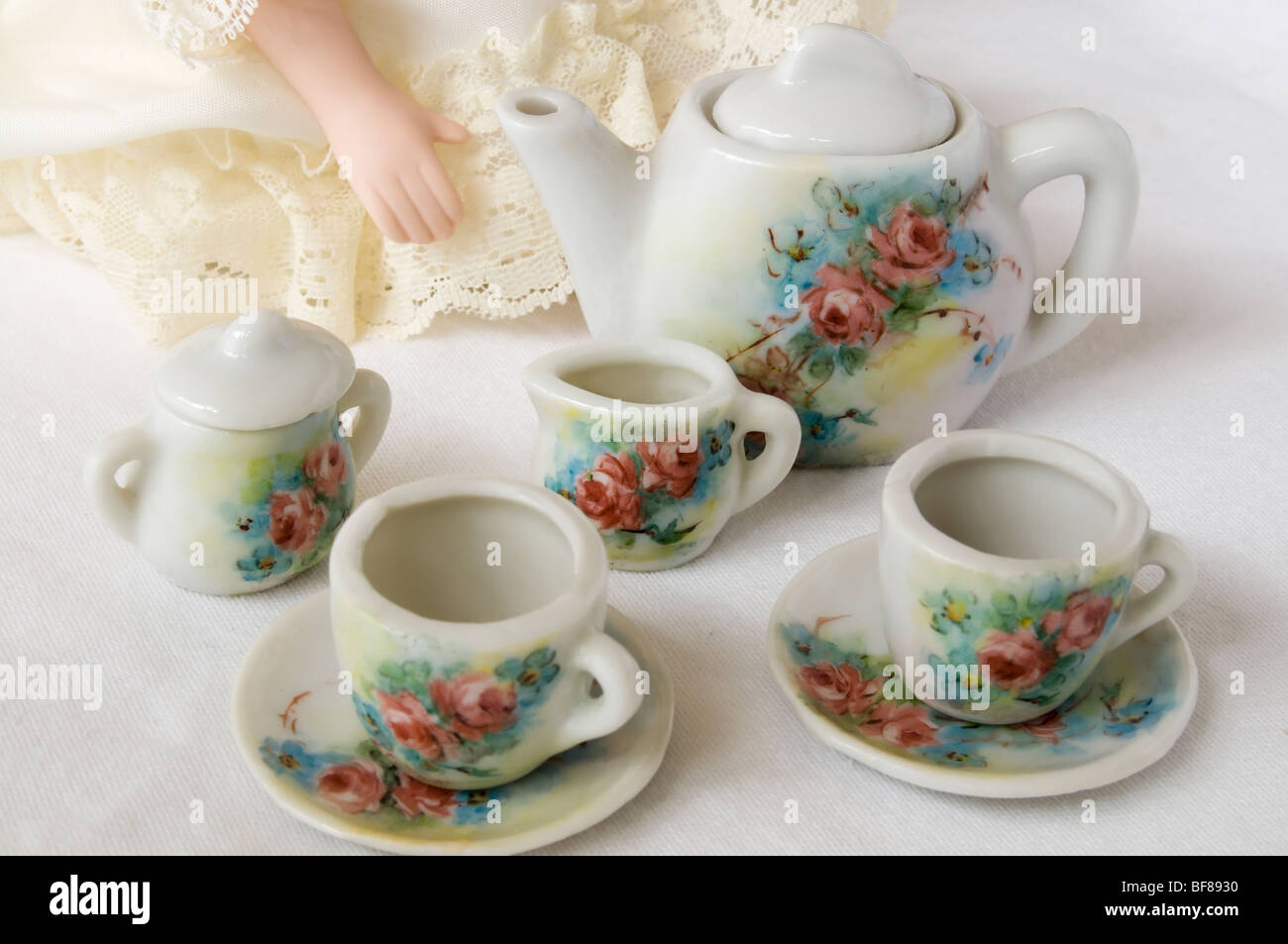 Closeup of miniature tea set painted with a floral design.  Portion of a doll can be seen in background. Stock Photo
