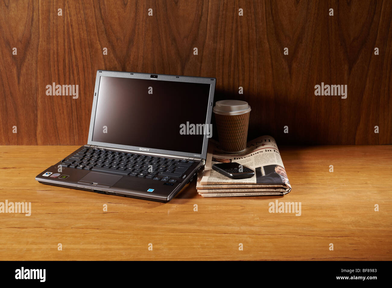 Laptop on desk with a Blackberry phone, coffee and financial newspaper. Stock Photo