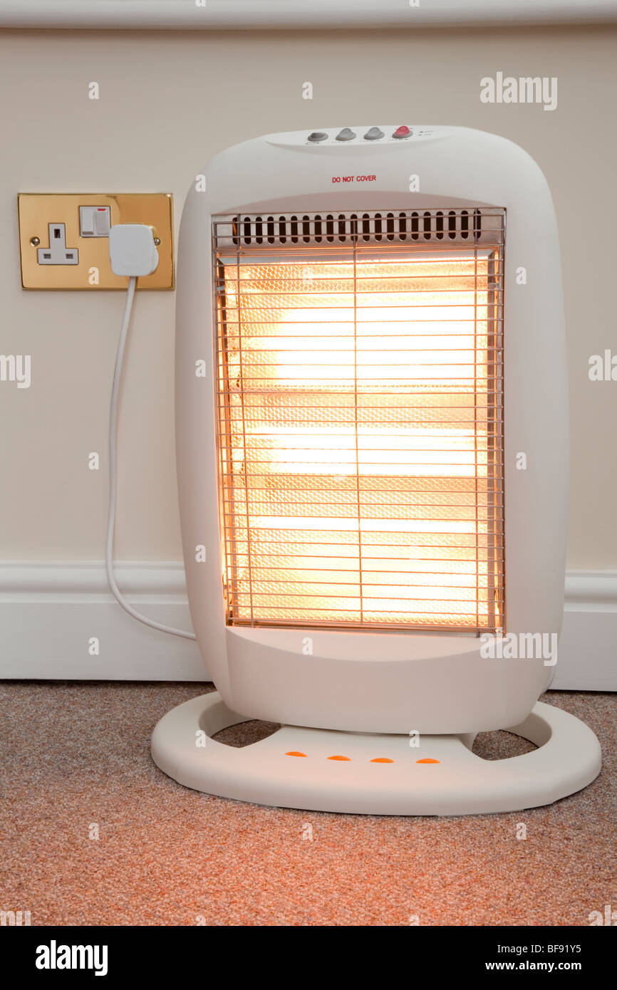 Electric halogen room heater with three heat settings plugged into electrical wall socket and switched on with high setting Stock Photo