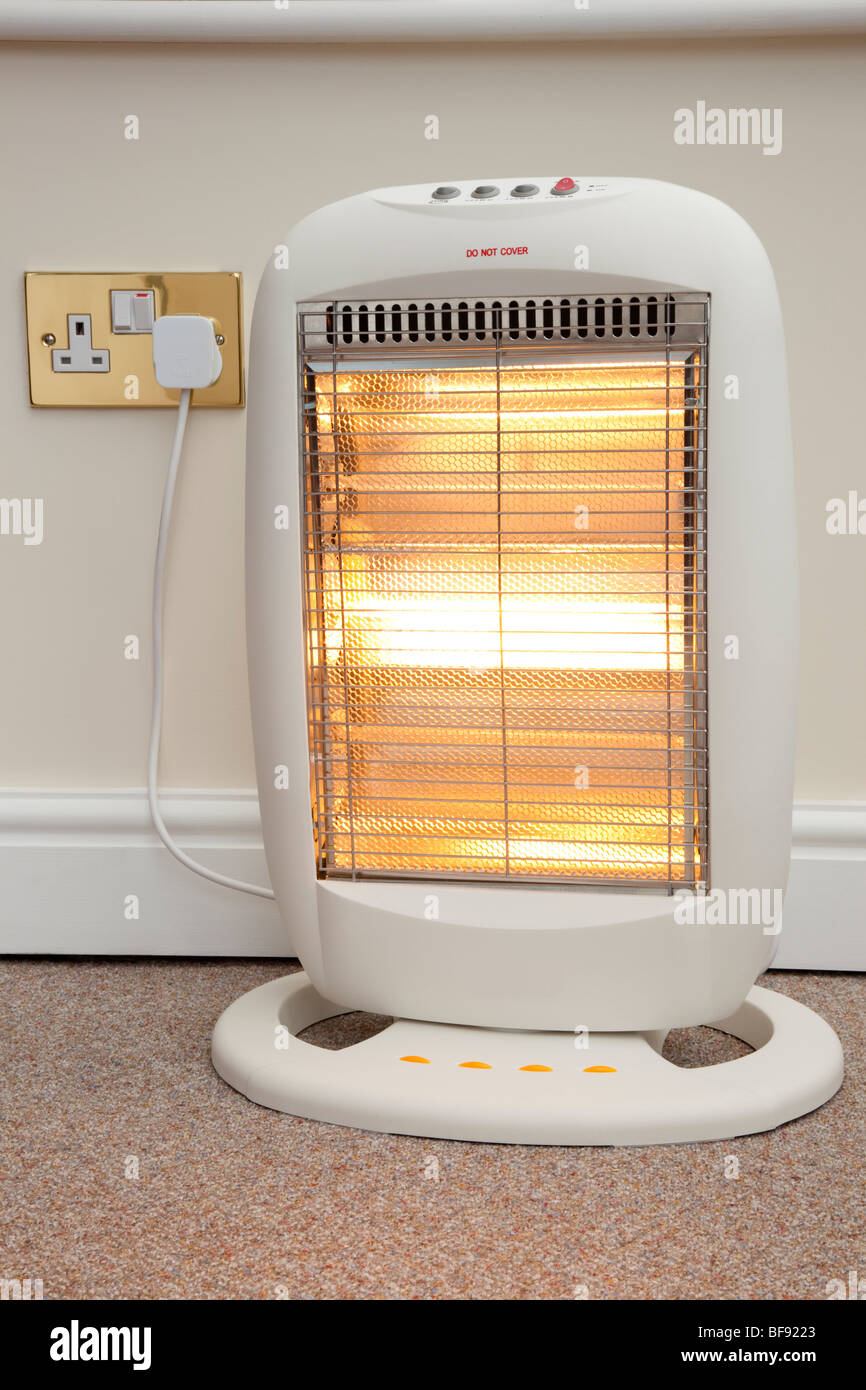 Domestic electric halogen room heater with three heat settings plugged into electrical wall socket and switched on with low setting in eco home. UK Stock Photo