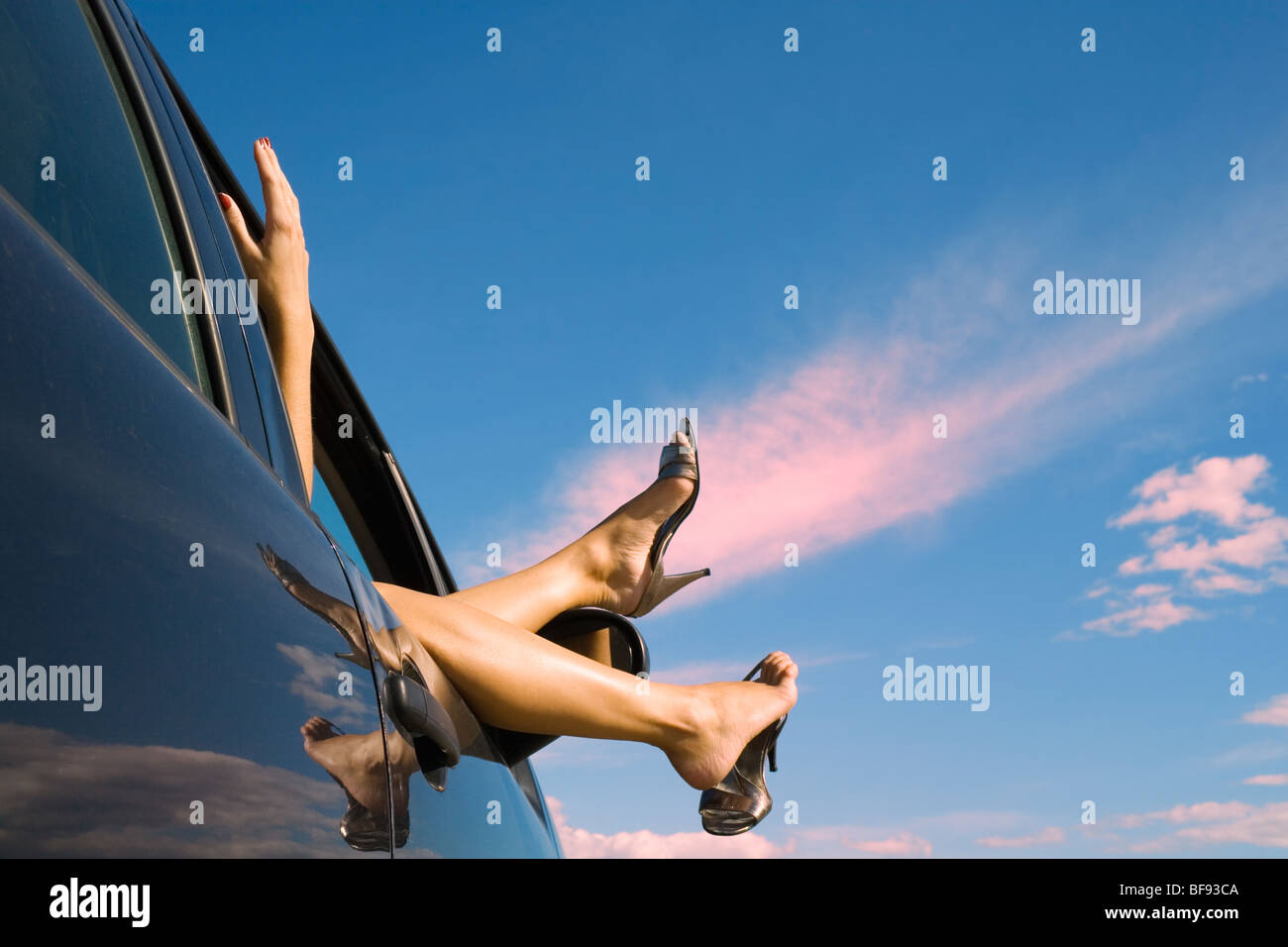 Woman's legs and feet wearing silver high heeled shoes sticking out of car window. Stock Photo