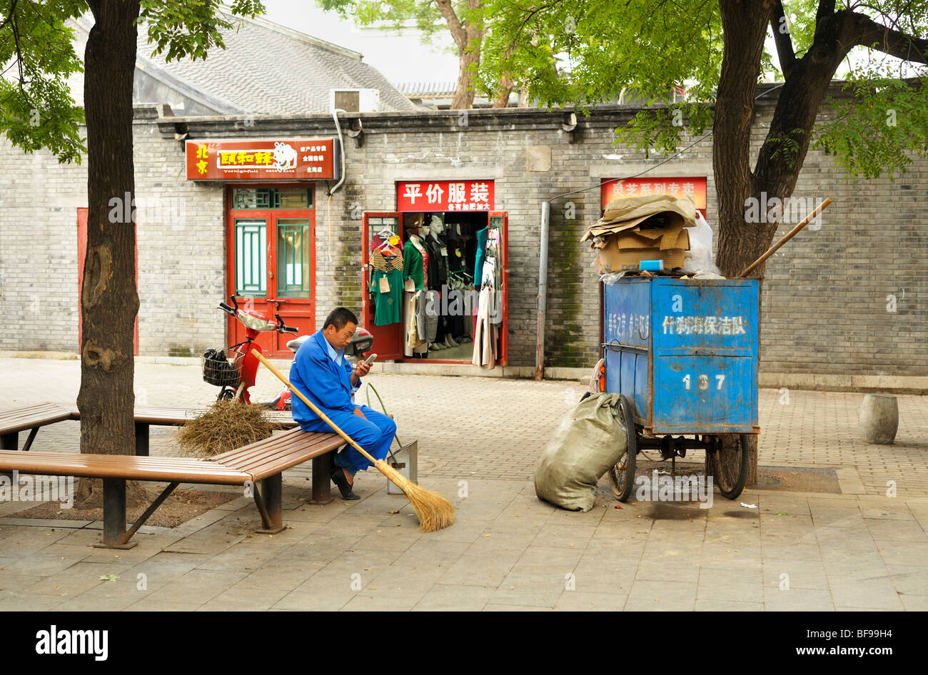 A street cleaner in blue uniform taking a break and checking messages on his mobile phone, Bejing CN Stock Photo