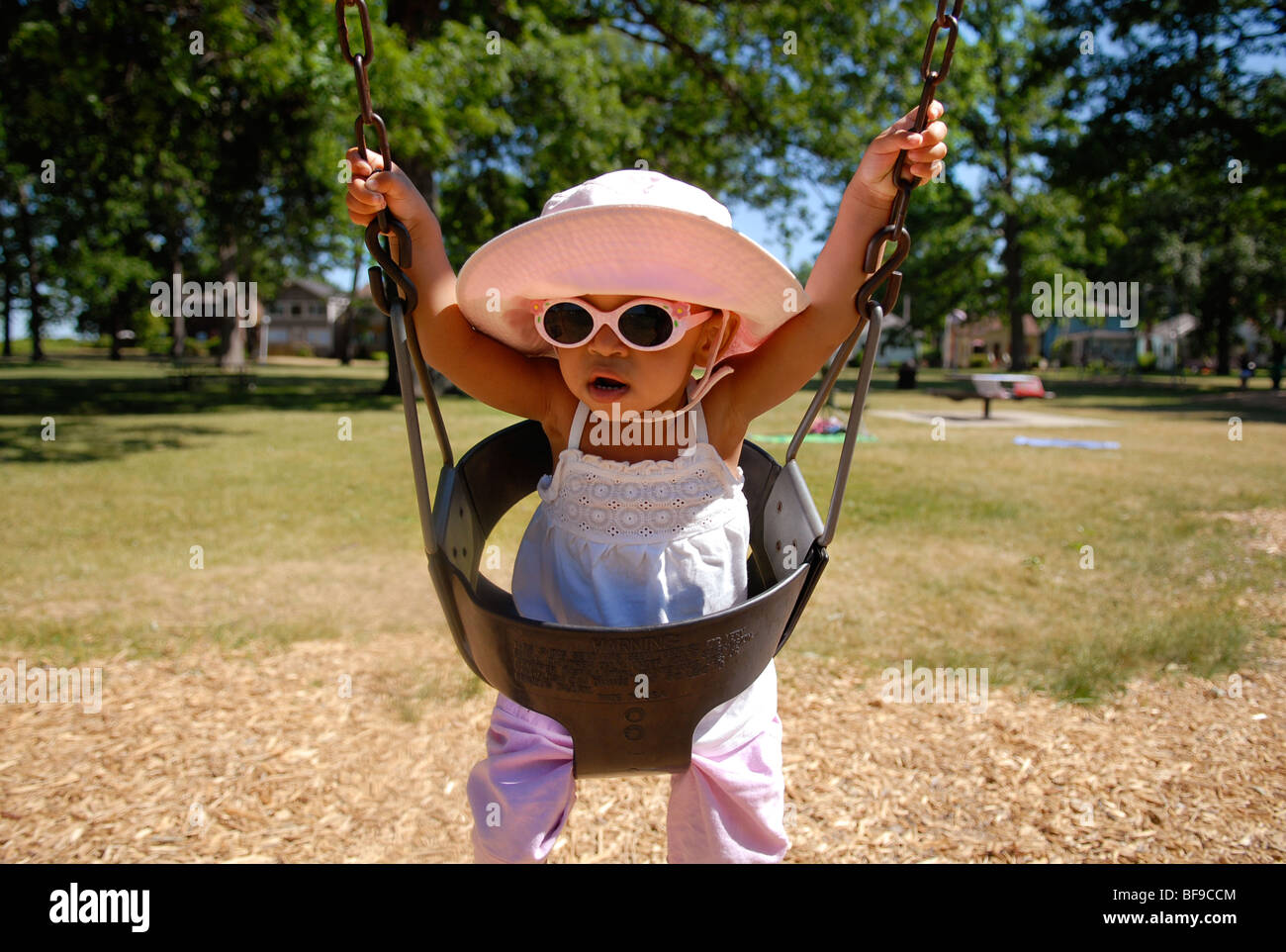 A toddler wearing a sun hat and sunglasses holds onto chains as she