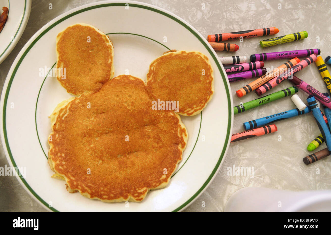 Crayons surround a child's mouse-shaped pancake on a stoneware plate during breakfast at a small diner. Stock Photo