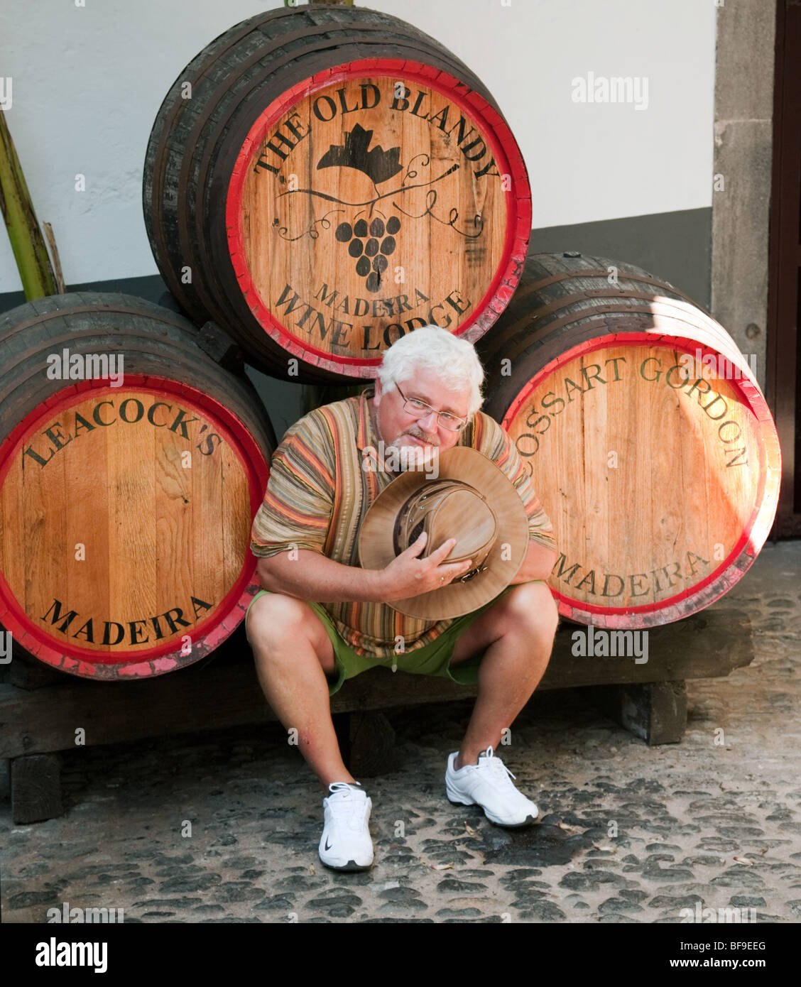 An elderly male tourist posing with Barrels of madeira wine, Blandys, Funchal, Madeira Stock Photo