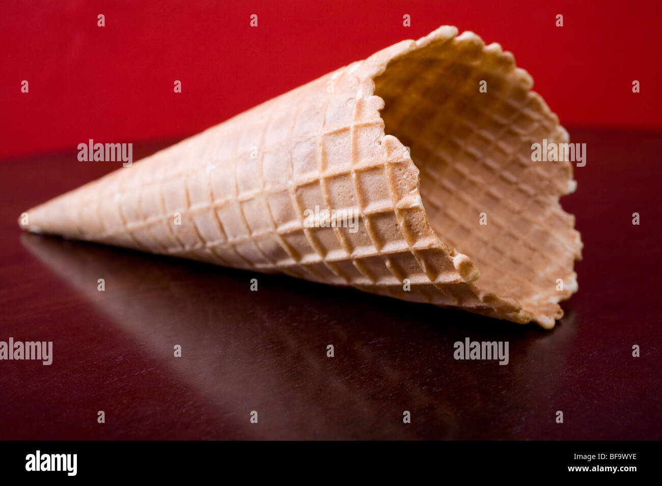 Quality ice cream cone on a brown table against a red wall. Stock Photo