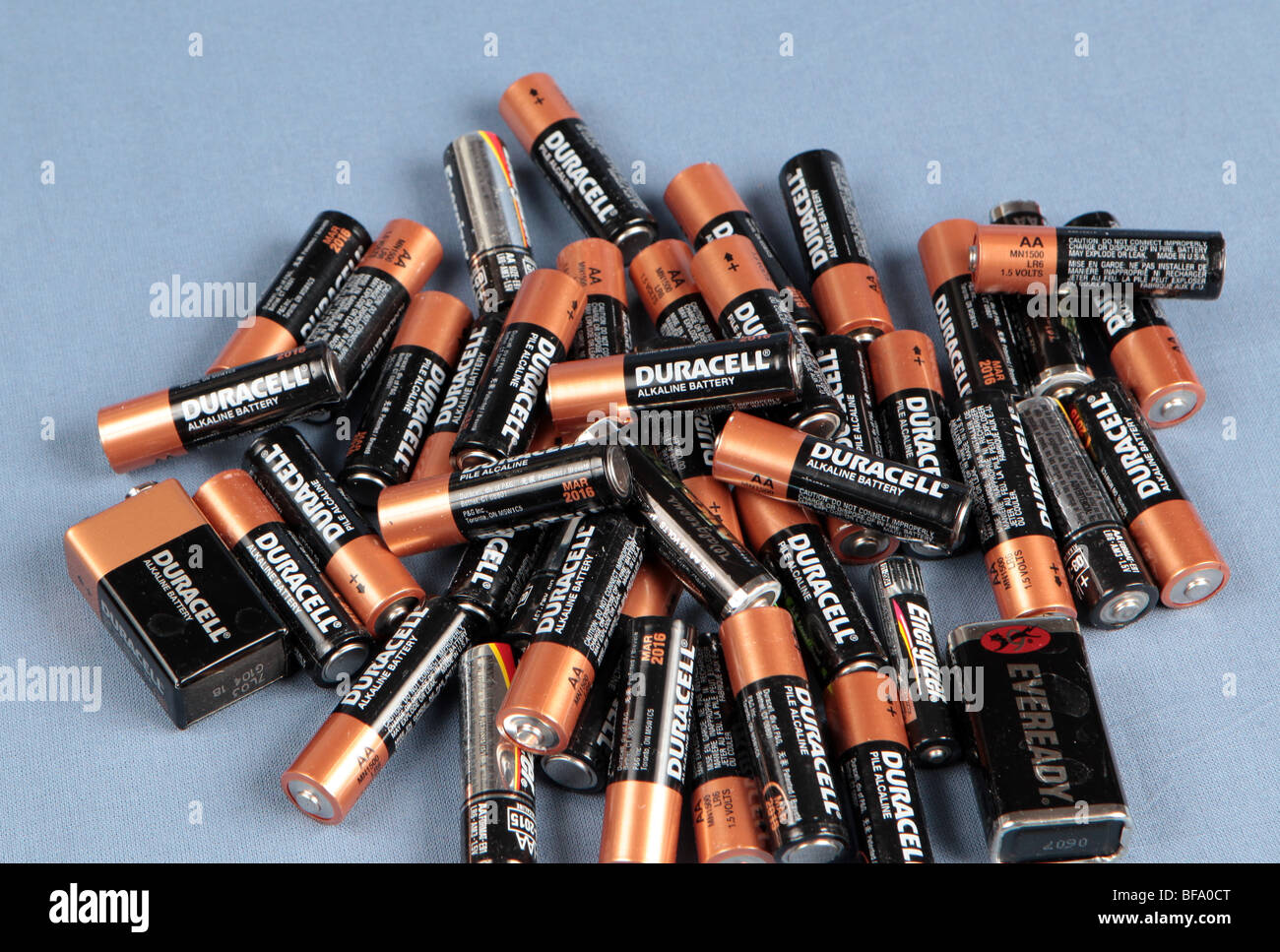 An pile of AA batteries piled on a table shot against a blue background