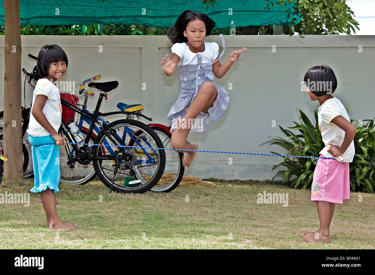 Youngsters playing in the garden and jumping a rope. Thailand S. E. Asia Stock Photo