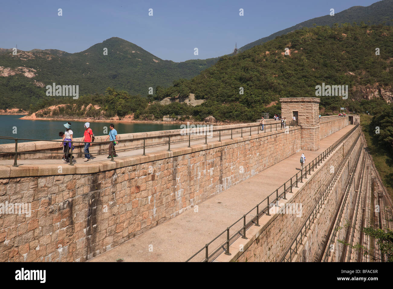 Hikers walking across a water reservoir wall in Tai Tam Country Park in Hong Kong. Stock Photo