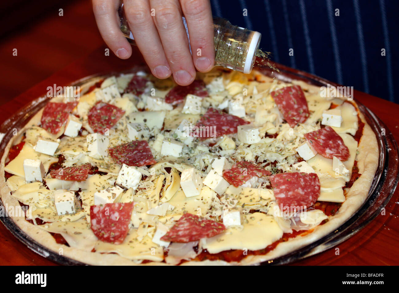 Sprinkling dried oregano oreganum on pizza. Stock Photo