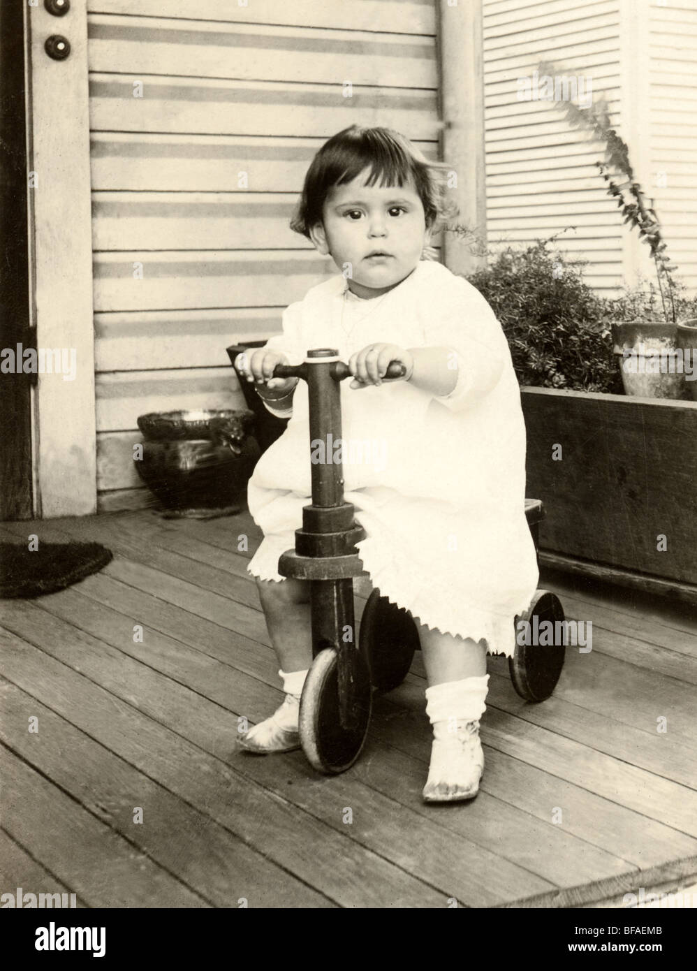 Infant Girl Riding Three-Wheel Scooter on Porch Stock Photo