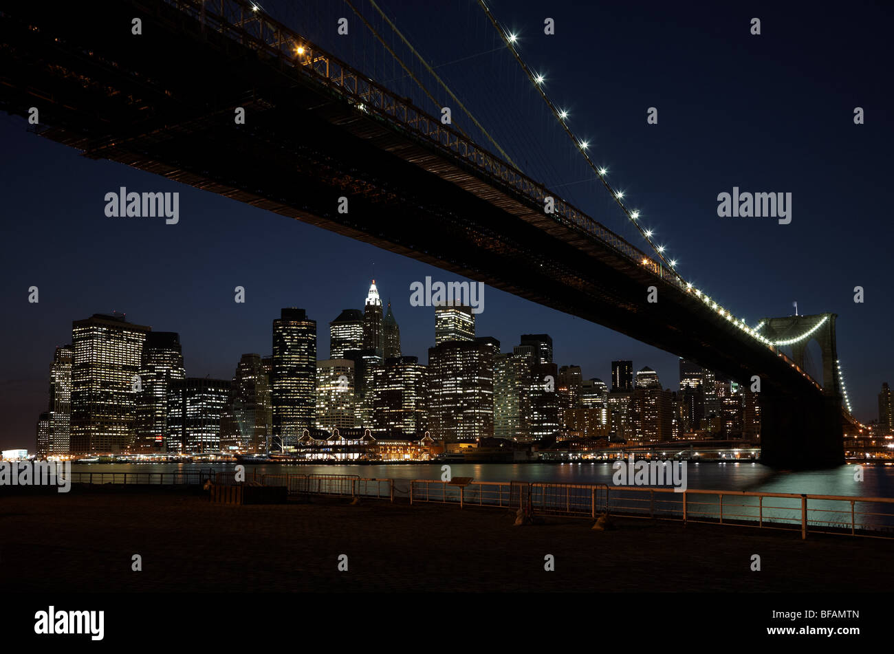 The view under Brooklyn Bridge towards the Lower Manhattan financial district, New York, at night. Stock Photo