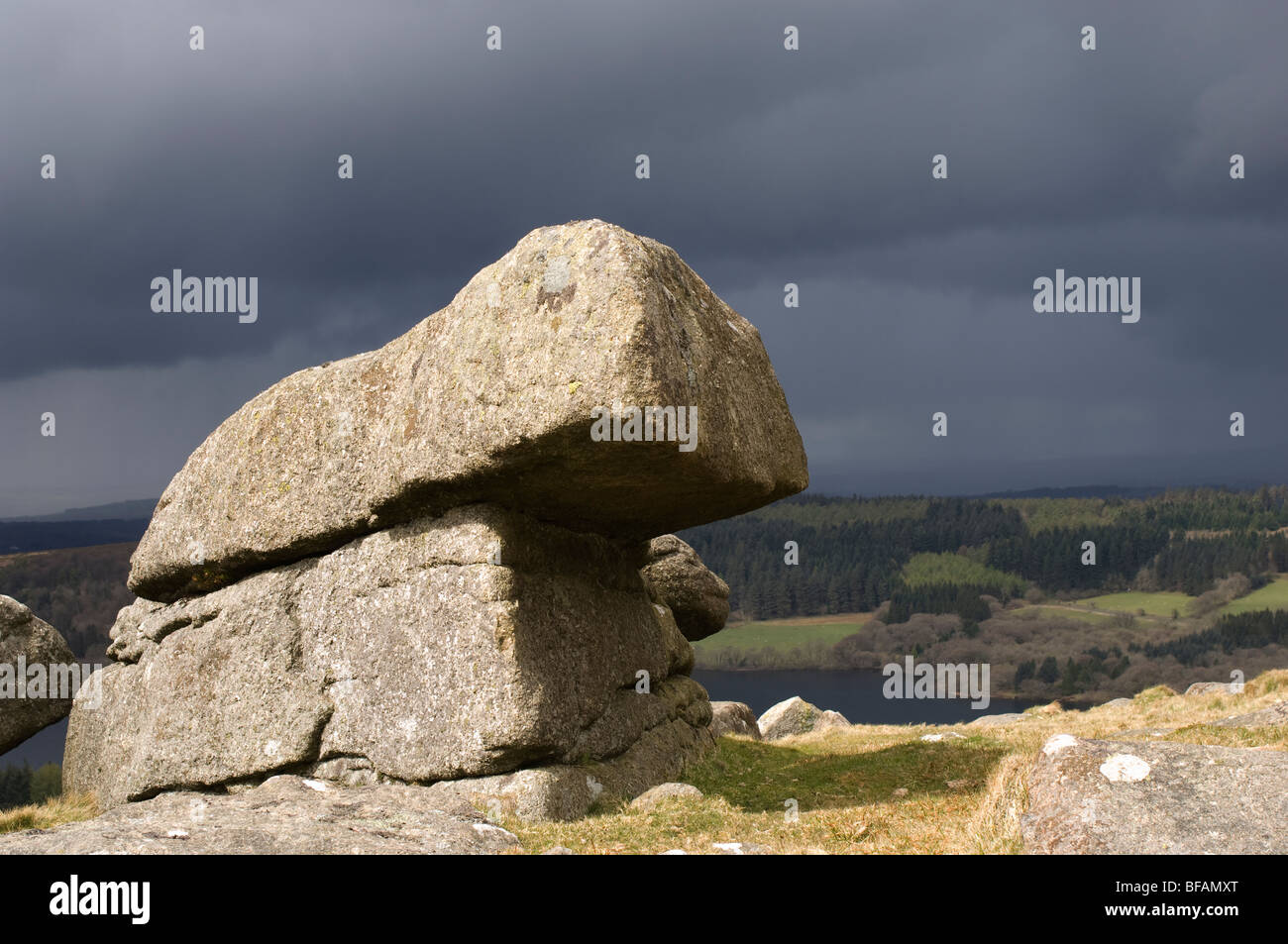 Sunlit granite rock formation with dark storm shower behind, Devon, UK Stock Photo