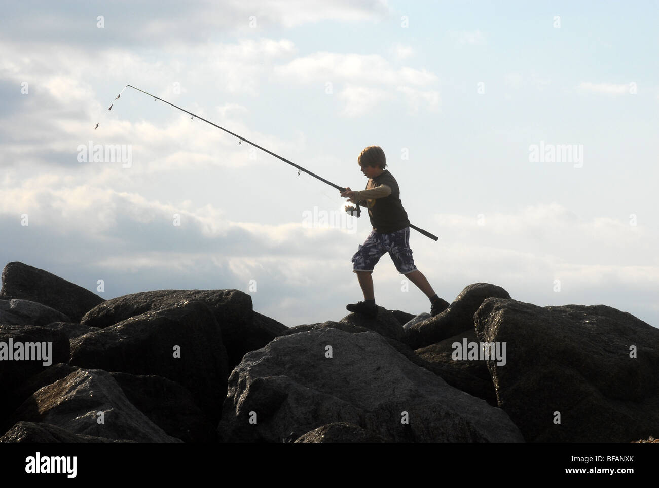 boy with fishing rod climbing over rocks Stock Photo