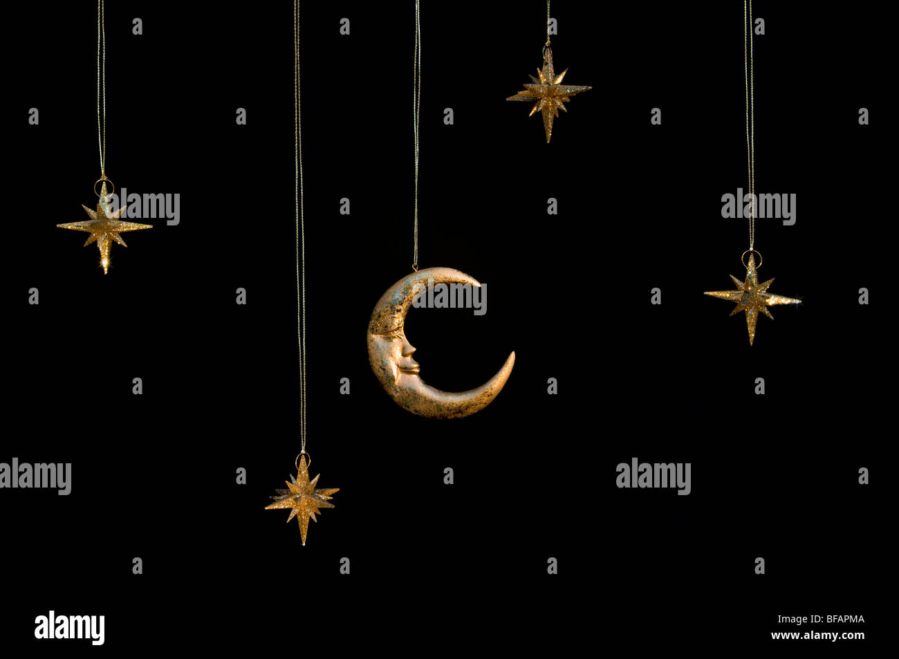 Gold shiny moon and stars sparkly hanging christmas decorations against a black background Stock Photo