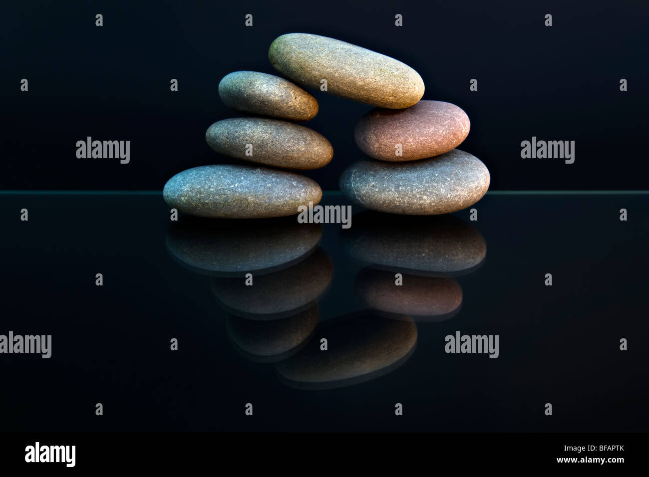 Still life shot of beach pebbles balanced in a stone pile against black background with reflection making a circular shape Stock Photo