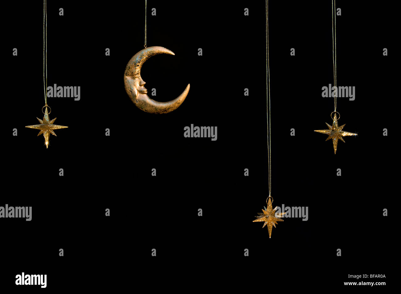 Gold shiny moon and stars sparkly hanging christmas decorations against a black background Stock Photo