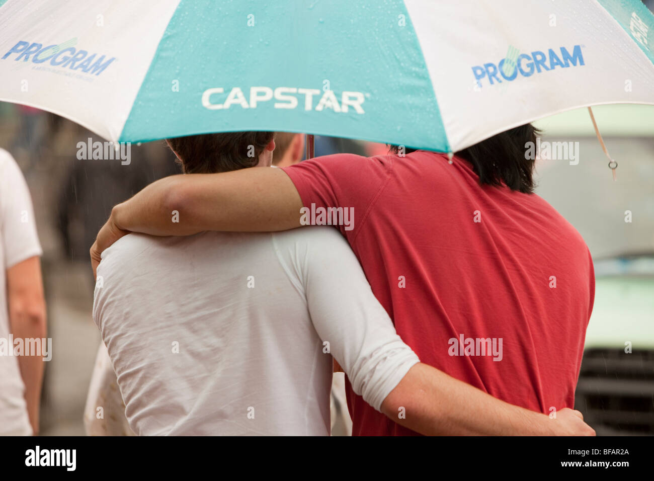 Two men sheltering under an umbrella in the rain. Stock Photo