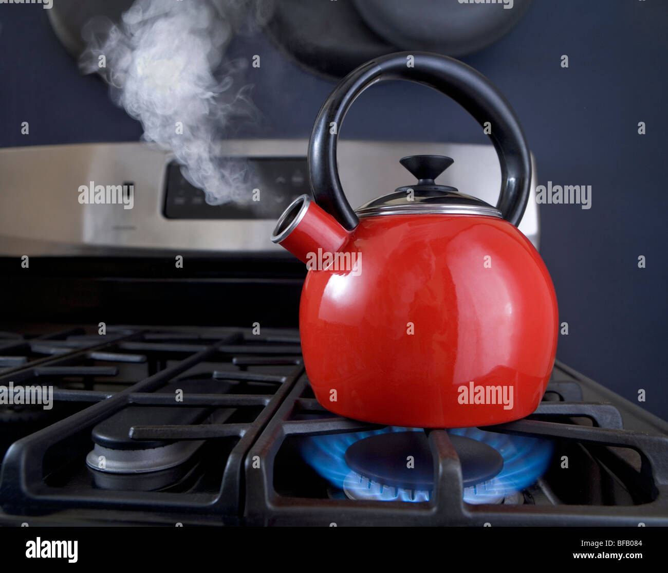 A red teapot is on the boil and steam is pouring out of the spout. Stock Photo