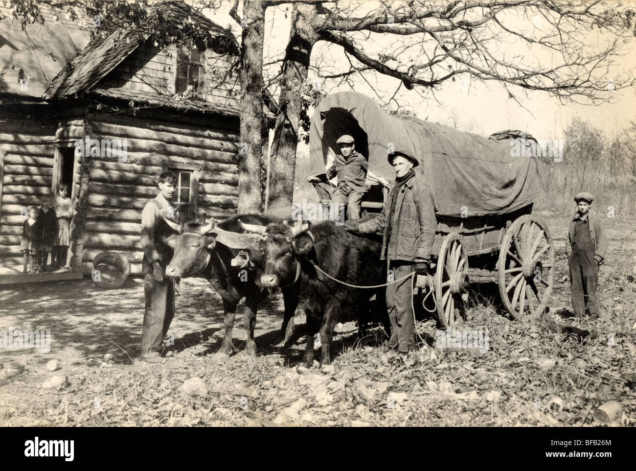 Family at Log Cabin with Covered Wagon Stock Photo