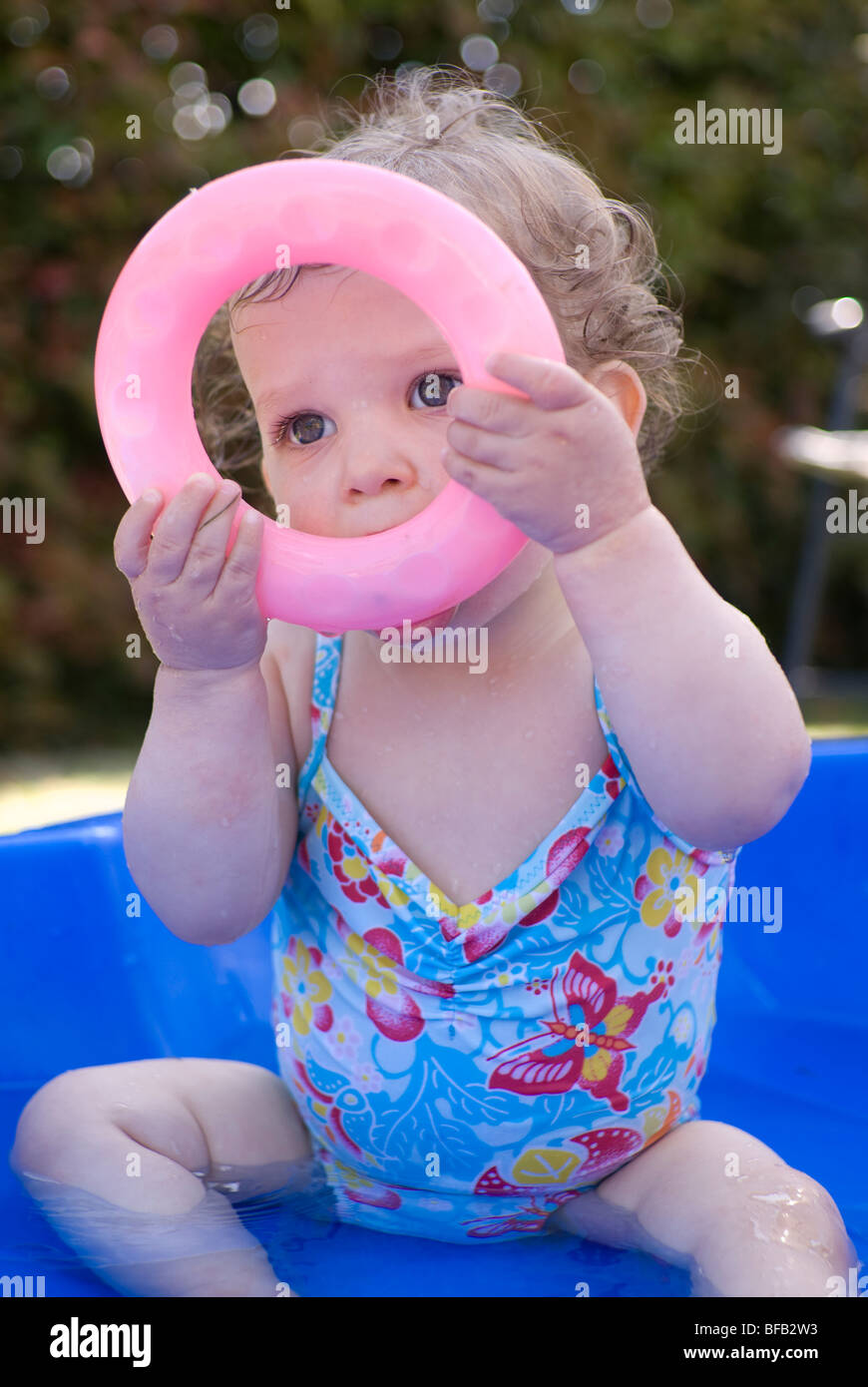16 month old girl playing in small back garden paddling pool. Stock Photo